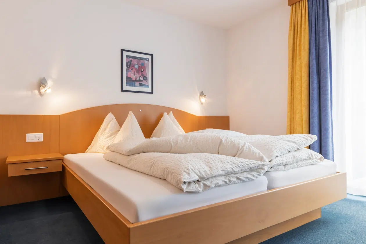 Ein sauber gemachtes Bett mit beiger Bettwäsche in einem hellen, modernen Schlafzimmer des Apartment Samnaun.