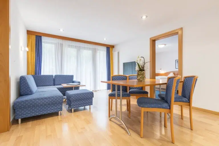 Modernes Apartment Samnaun Wohn- und Essbereich mit blauen Möbeln, Holz und grossen Fenstern.