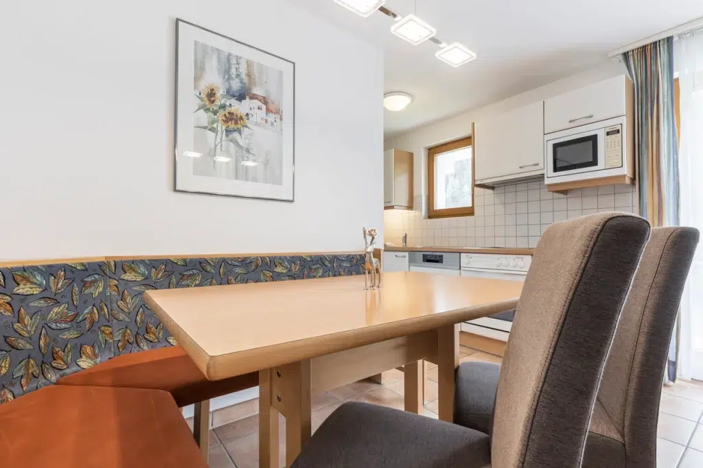 Esstisch mit Stühlen in der hellen Küche des Apartments Samnaun, dahinter ein Kunstwerk und ein Fenster.