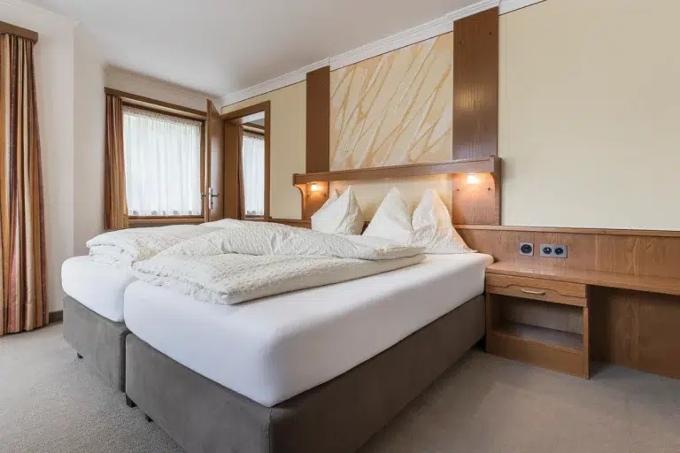 Doppelzimmer Samnaun mit zwei Einzelbetten, weißem Bettzeug und warmen Holzakzenten.