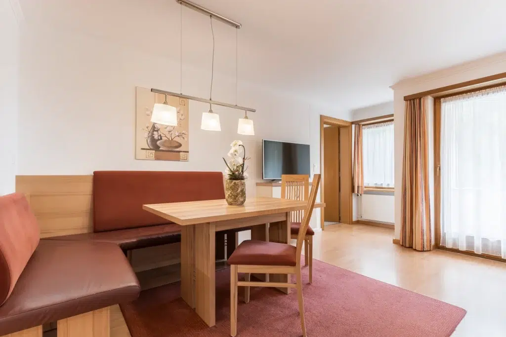Moderner Essbereich im Apartment Samnaun mit Holztisch, roter Sitzbank und grossen Fenstern.