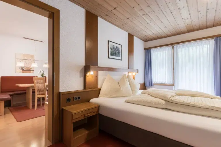 Gemütliches Schlafzimmer mit Doppelbett, Nachttisch und Blick in den Essbereich von Apartment Samnaun.