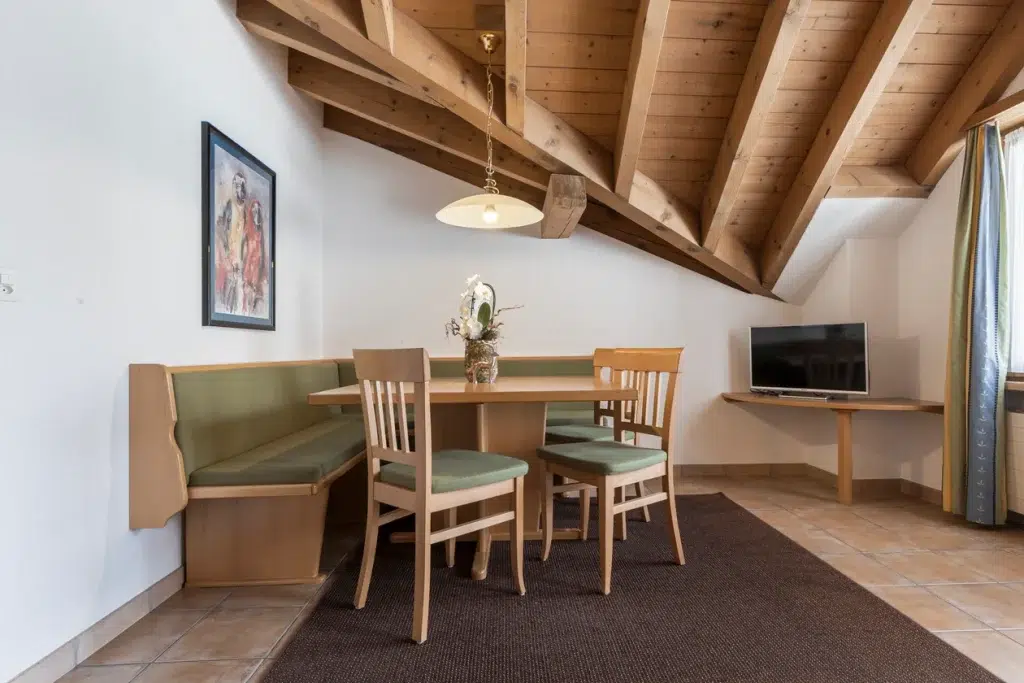 Essecke im Appartement Samnaun mit Holztisch, Stühlen, Eckbank, TV und Dachschräge.