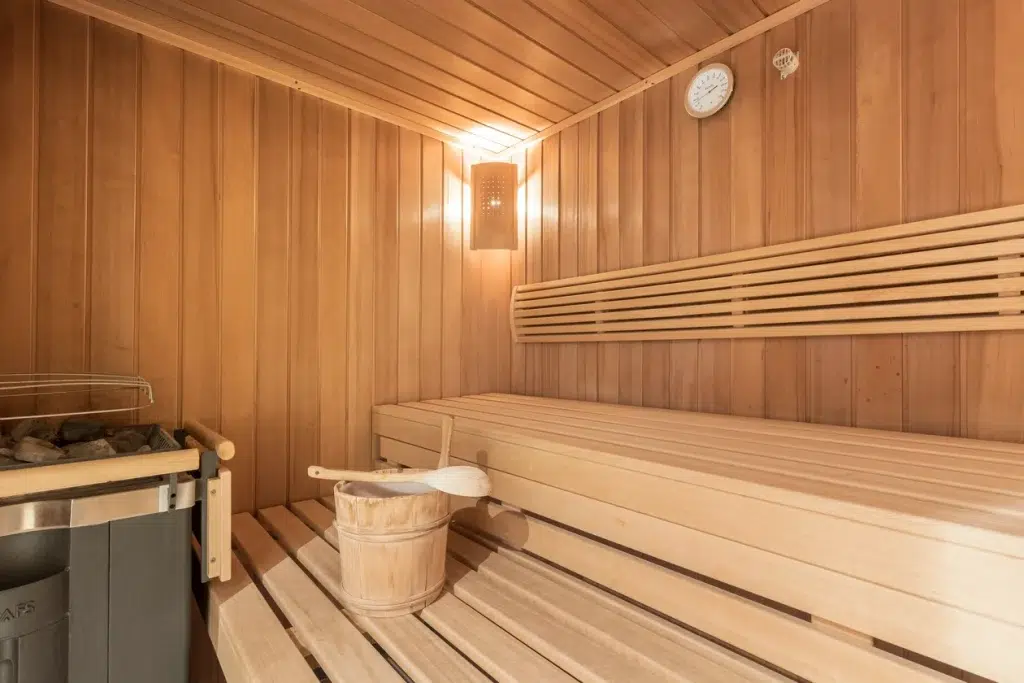 Hölzerne Saunakabine im Ferienhaus Samnaun mit Bank, Eimer, Schöpfkelle, Ofen, Licht und Uhr.