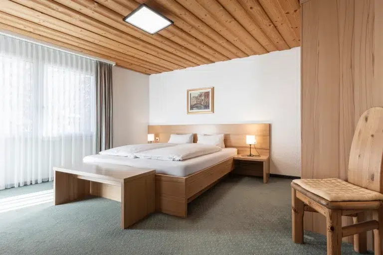 Minimalistisches Schlafzimmer im Apartment Samnaun mit Holzmöbeln, Doppelbett und transparenten Vorhängen.