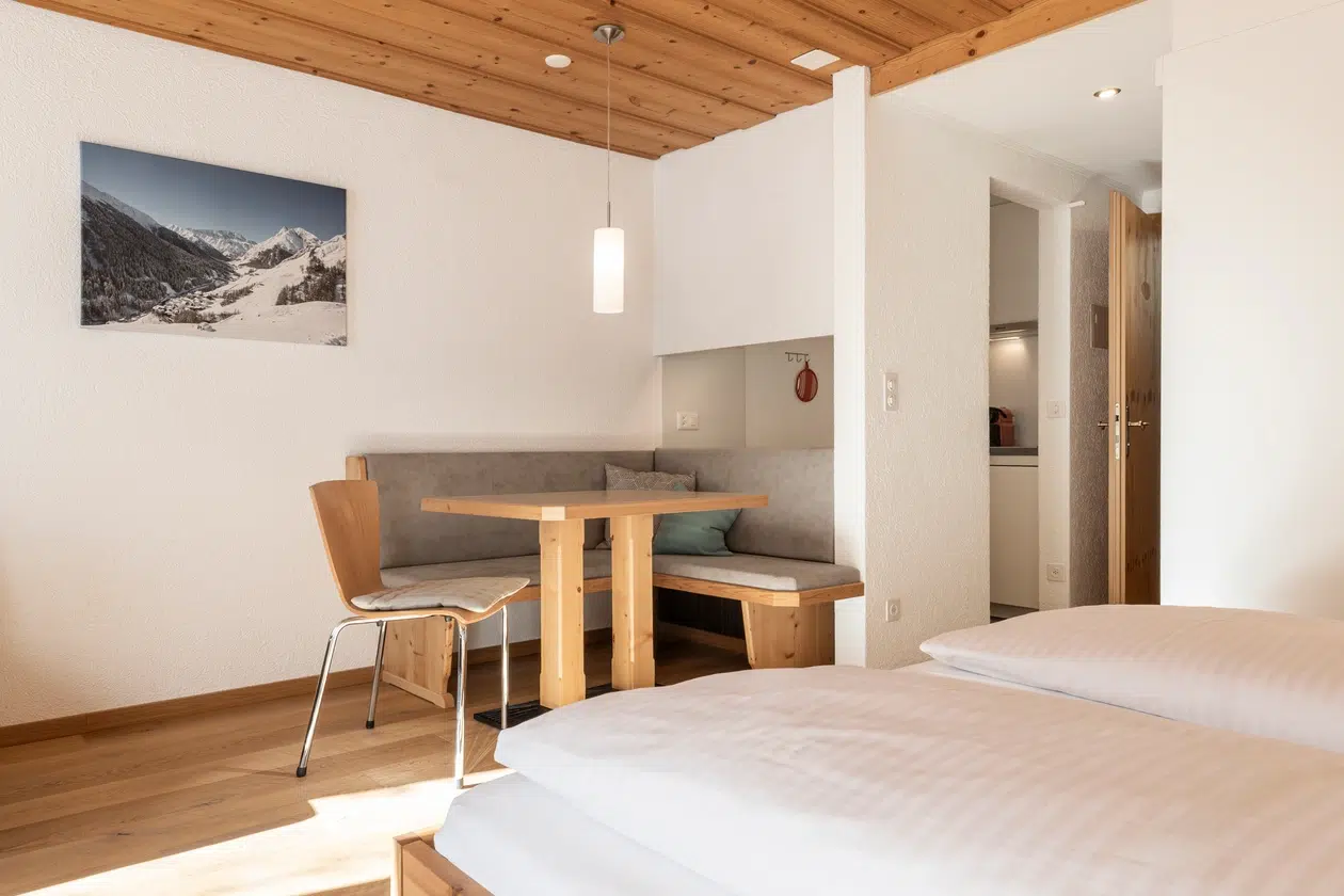 Gemütliches Appartement Samnaun Zimmer mit Holztisch, Sitzbank, Bett und Bergfoto an der Wand.