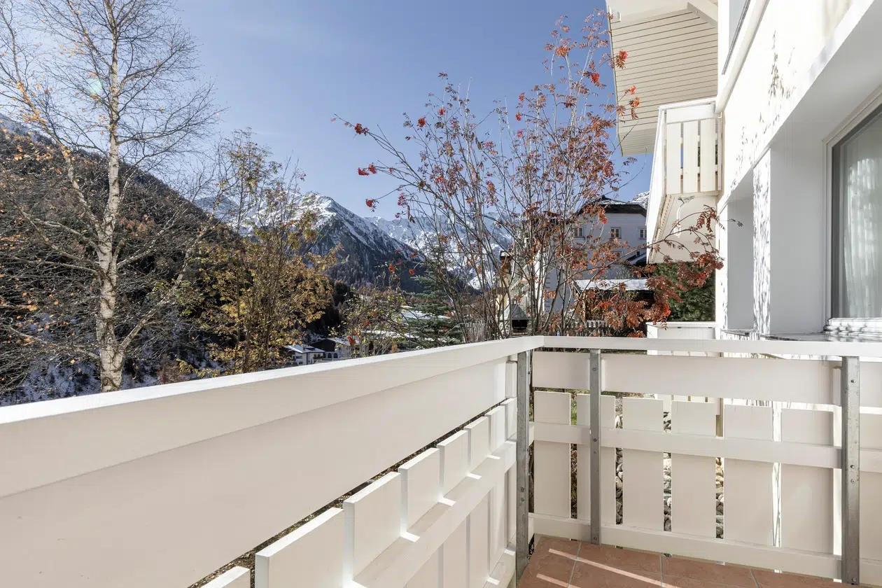 Weisser Balkon im Apartment Samnaun mit Blick auf Berge und Bäume an einem klaren, sonnigen Tag.