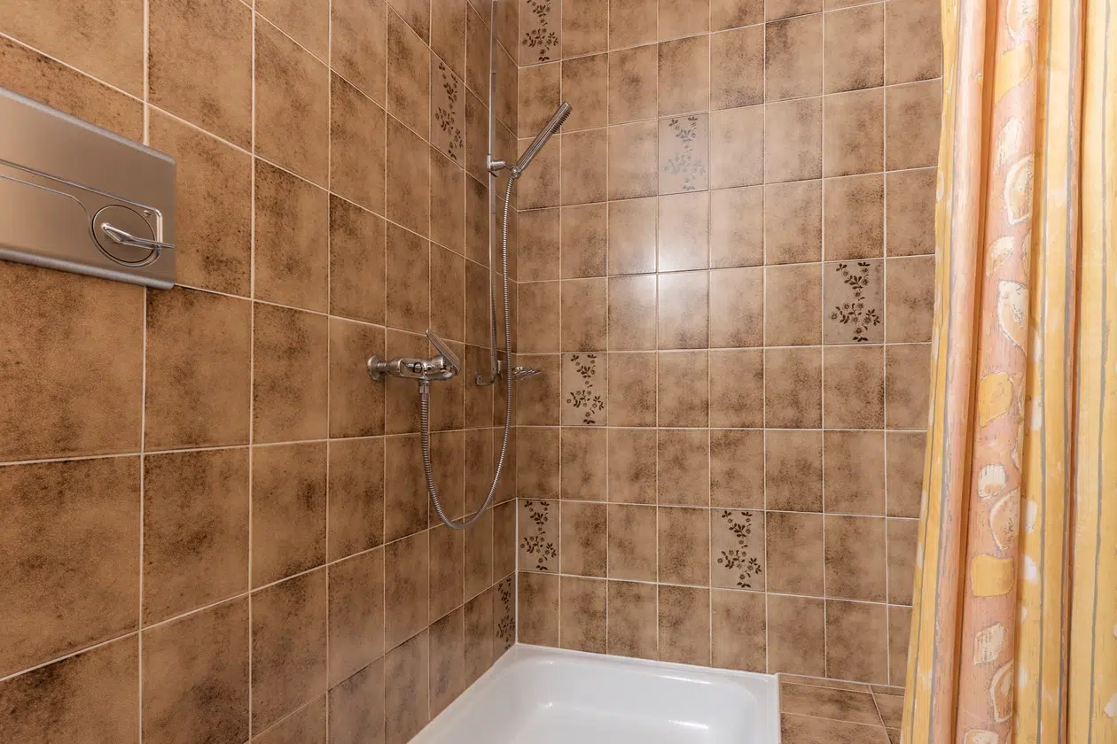 Dusche im Apartment Samnaun mit braun gemusterten Fliesen und einem gelb gemusterten Vorhang.