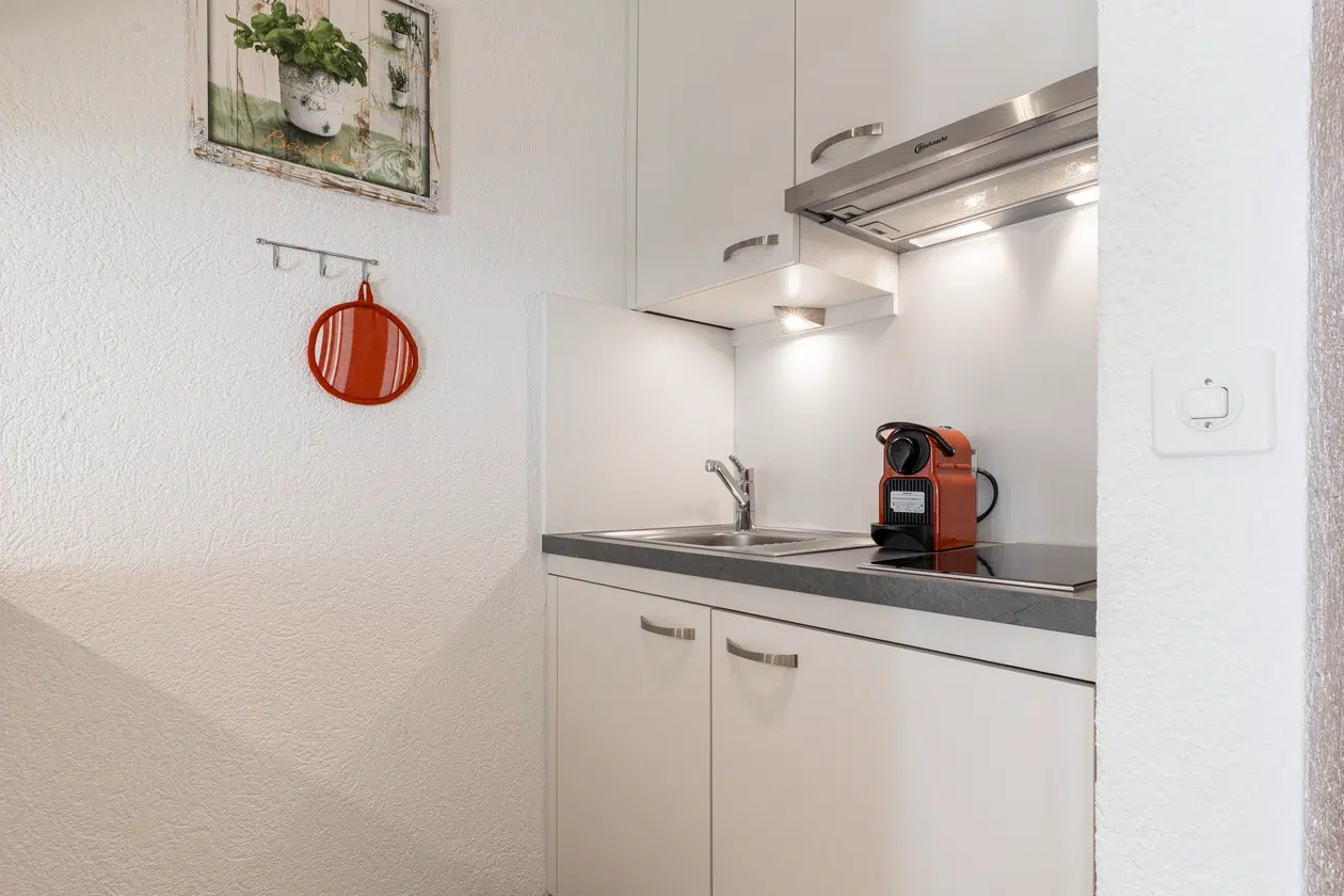 Kleine weiße Küche im Apartment Samnaun mit Spüle, roter Kaffeemaschine und Wandkunst darüber.