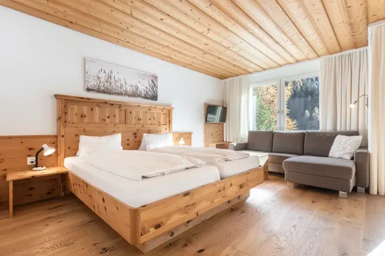 Gemütliches Holzzimmer im Apartment Samnaun mit Doppelbett, Sofa und Blick in die Natur.