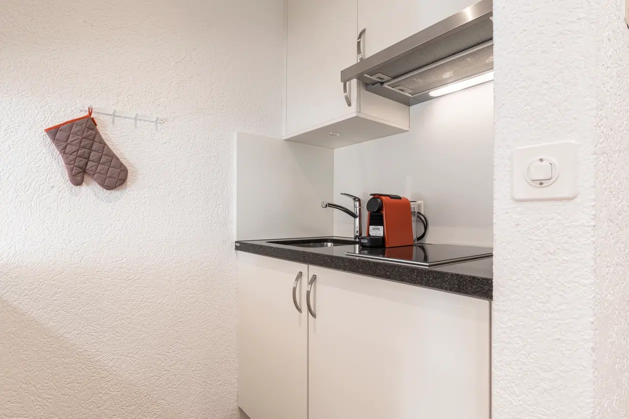 Gemütliche weisse Küchenzeile im Appartement Samnaun mit Kaffeemaschine, Spülbecken und Topflappen.