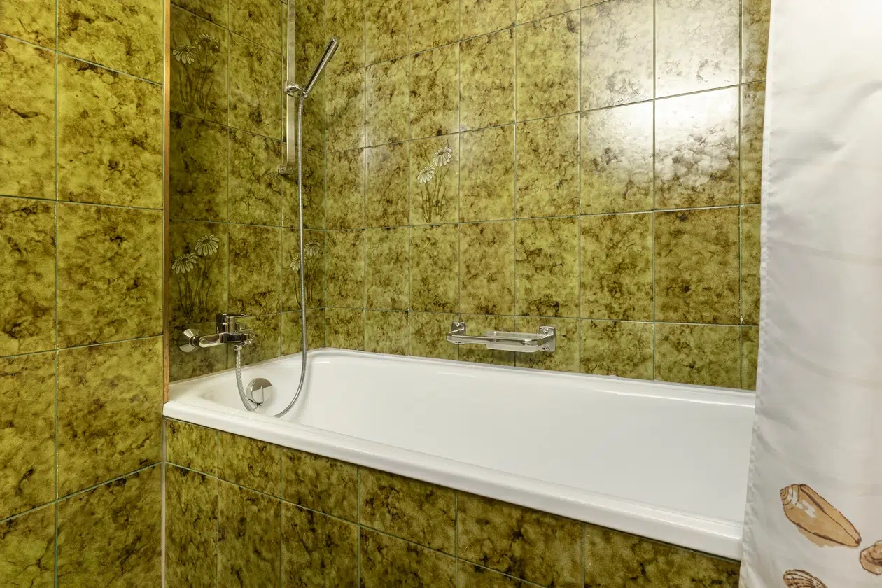 Grün gefliestes Badezimmer im Apartment Samnaun mit weißer Badewanne und teilweise sichtbarem Duschvorhang.