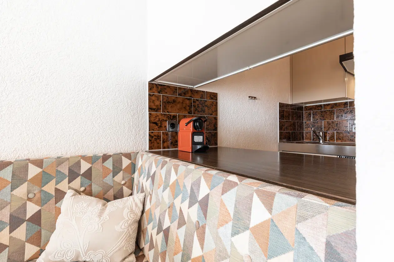 Geometrisch gemusterte Bank in der Wohnung Samnaun neben einem Küchentisch mit roter Kaffeemaschine.