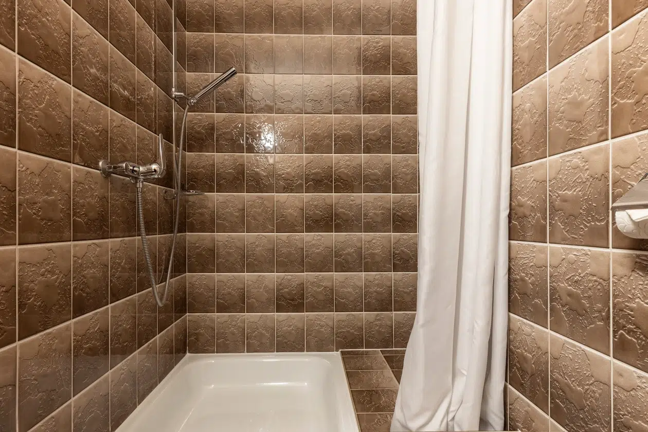 Wohnung Samnaun Dusche mit braun gefliesten Wänden, weißem Vorhang und Handbrause.