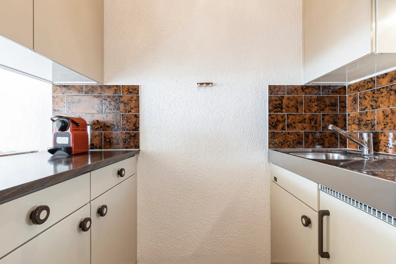 Kleine Küche im Apartment Samnaun mit braunem Backsplash, weißen Schränken und Kaffeemaschine.