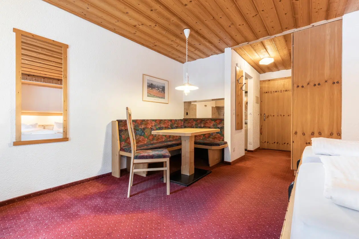Gemütliches Apartment Samnaun mit Holzdecke, rotem Teppich und einer Essecke.