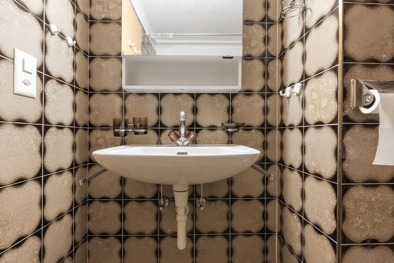 Kleines Badezimmer im Apartment Samnaun mit Wandwaschbecken und braun gemusterten Fliesen.