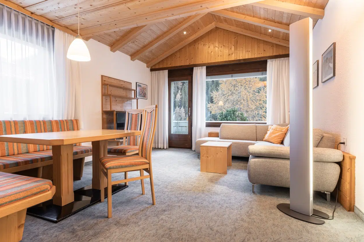 Gemütliches Apartment Samnaun Wohnzimmer mit Holzdecke, Essecke, Sofa und Blick auf die Bäume.