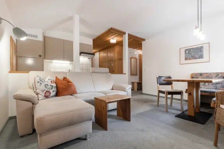 Gemütliches Wohnzimmer mit beigem Sofa, Holzmöbeln und Essecke im Appartement Samnaun.