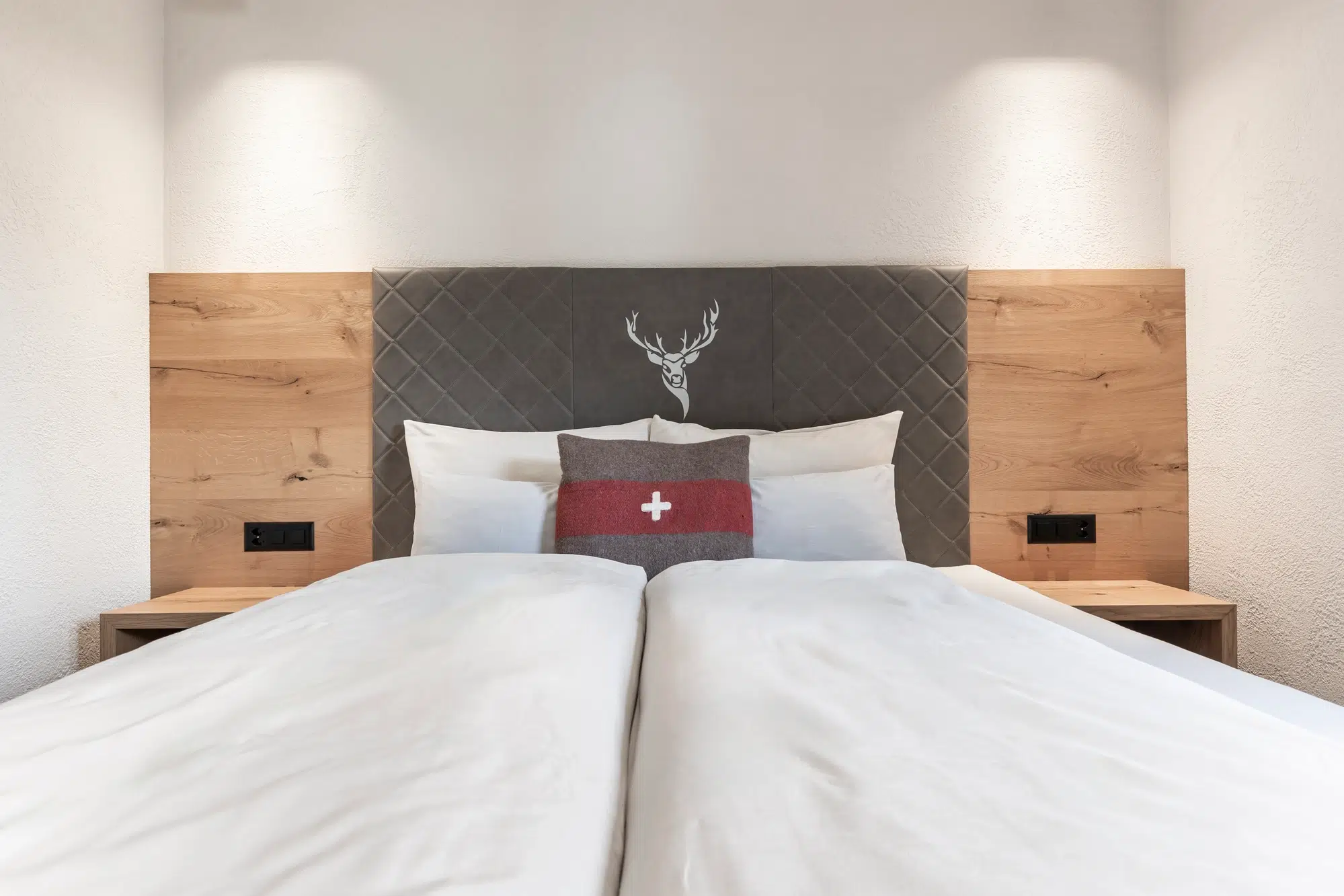 Gemachtes Bett mit weißer Bettwäsche, Holzkopfteil und einem roten Schweizer Kissen im Ferienhaus Samnaun.