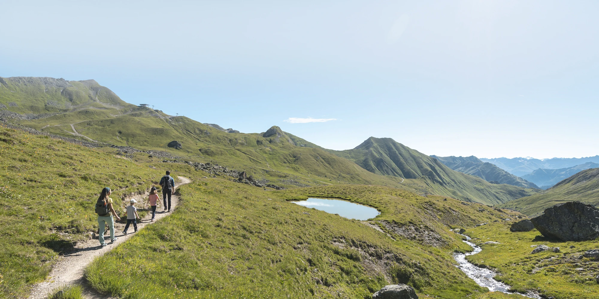 Eine Familie geniesst eine Familienurlaub Samnaun Sommer-Wanderung an einem Weiher unter freiem Himmel.