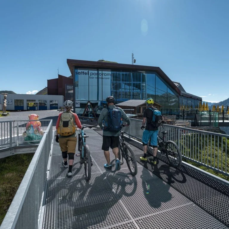 Drei Radfahrer fahren mit ihren Rädern auf ein modernes Glasgebäude zu und genießen das Biken Samaun.