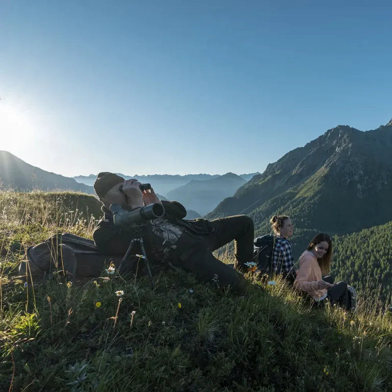 Drei Personen entspannen sich auf einer grasbewachsenen Anhöhe nach einem Trailrunning in den malerischen Bergen von Samnaun.