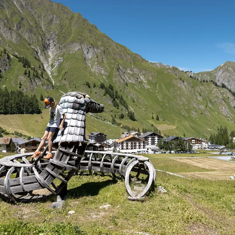 Eine Person steht auf einer Drachenskulptur in den Bergen und genießt den Familienurlaub Samnaun Sommer.
