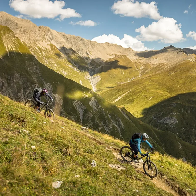 Zwei Personen genießen das Biken samaun an einem grasbewachsenen Hang mit Bergen im Hintergrund.