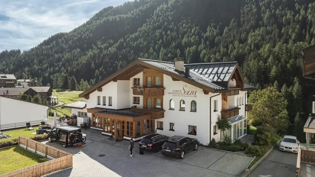 Ein Hotel im Chalet-Stil, Ferienhaus Samnaun, mit geparkten Autos und einer bewaldeten Bergkulisse.