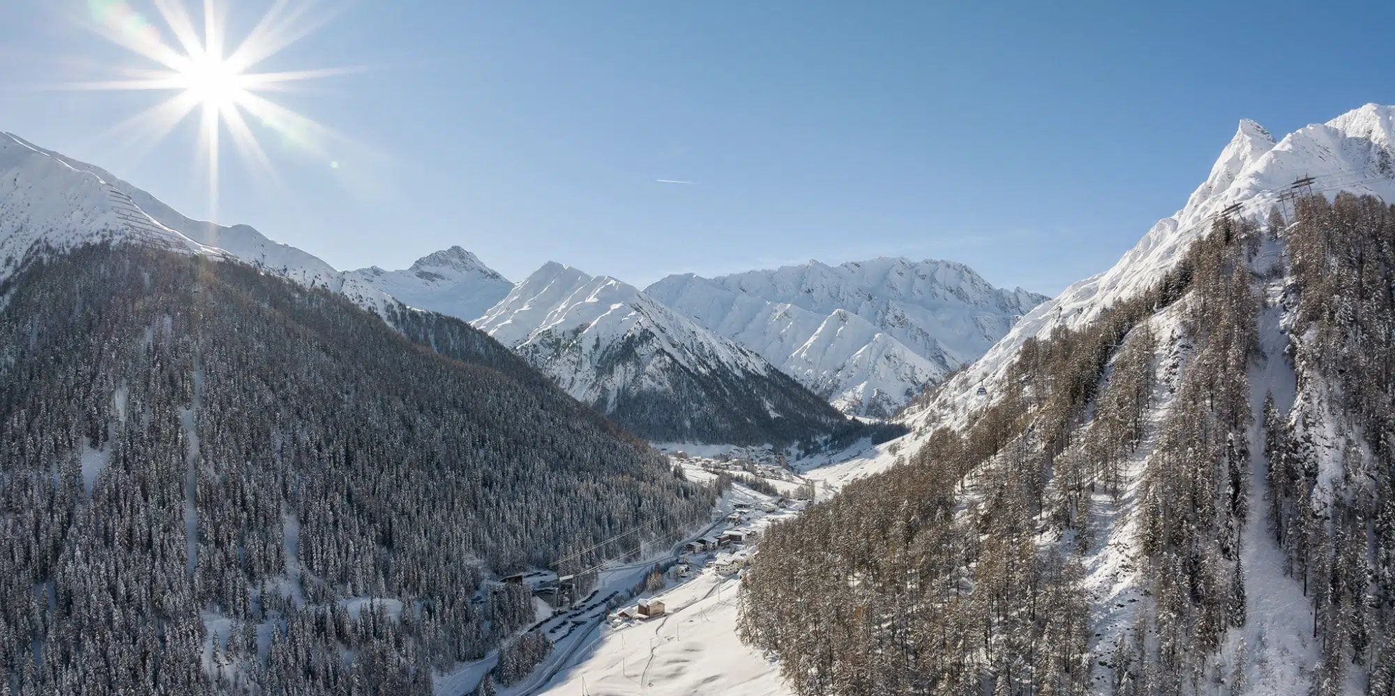 Verschneite Berge und bewaldetes Tal unter der strahlenden Sonne bei den Apartments Samnaun.