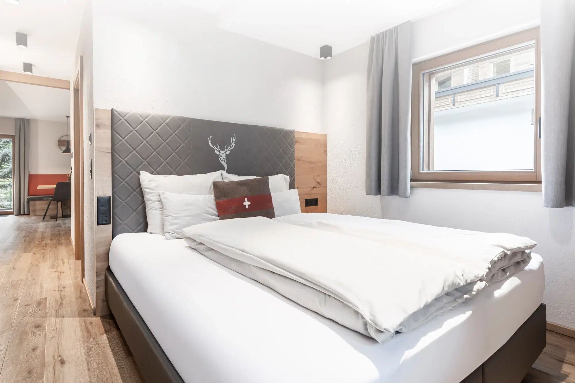 Modernes, helles Schlafzimmer unterkunft Samnaun mit Doppelbett, grauem Kopfteil und Fenster.