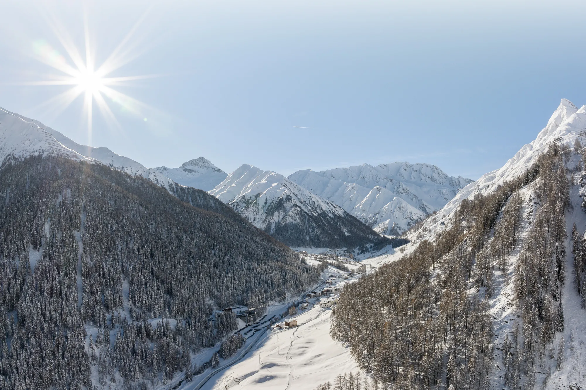 Schneebedeckte Berge und ein sonnenbeschienenes Tal mit unterkunft samnaun inmitten der Bäume.