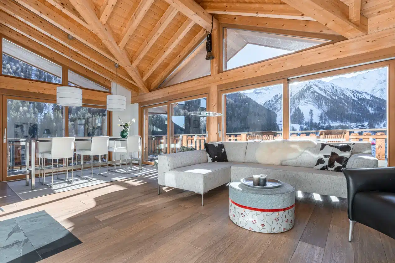 Modernes Wohnzimmer mit großen Fenstern, Holzdecke und Bergblick im Hintergrund.