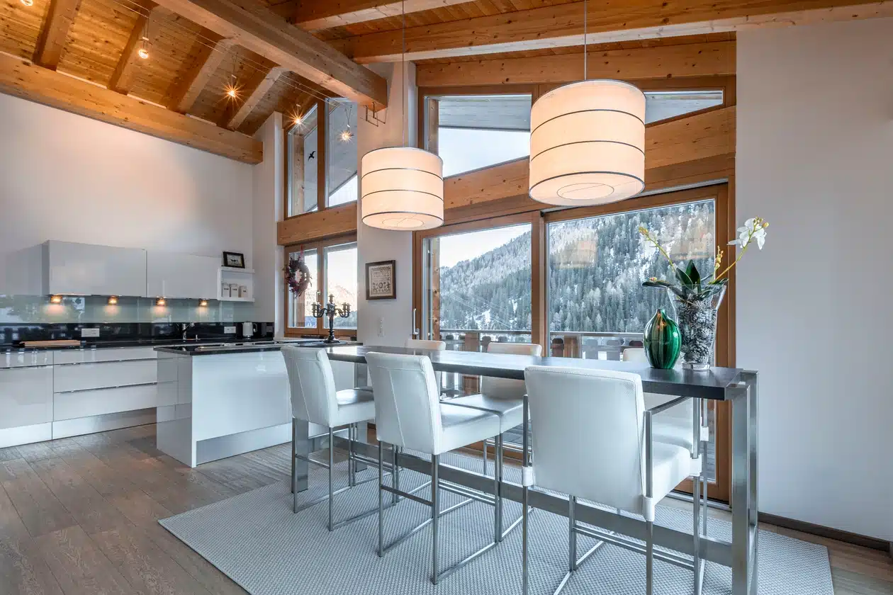 Moderne Küche und Essbereich mit großen Fenstern und Blick auf eine verschneite Berglandschaft.