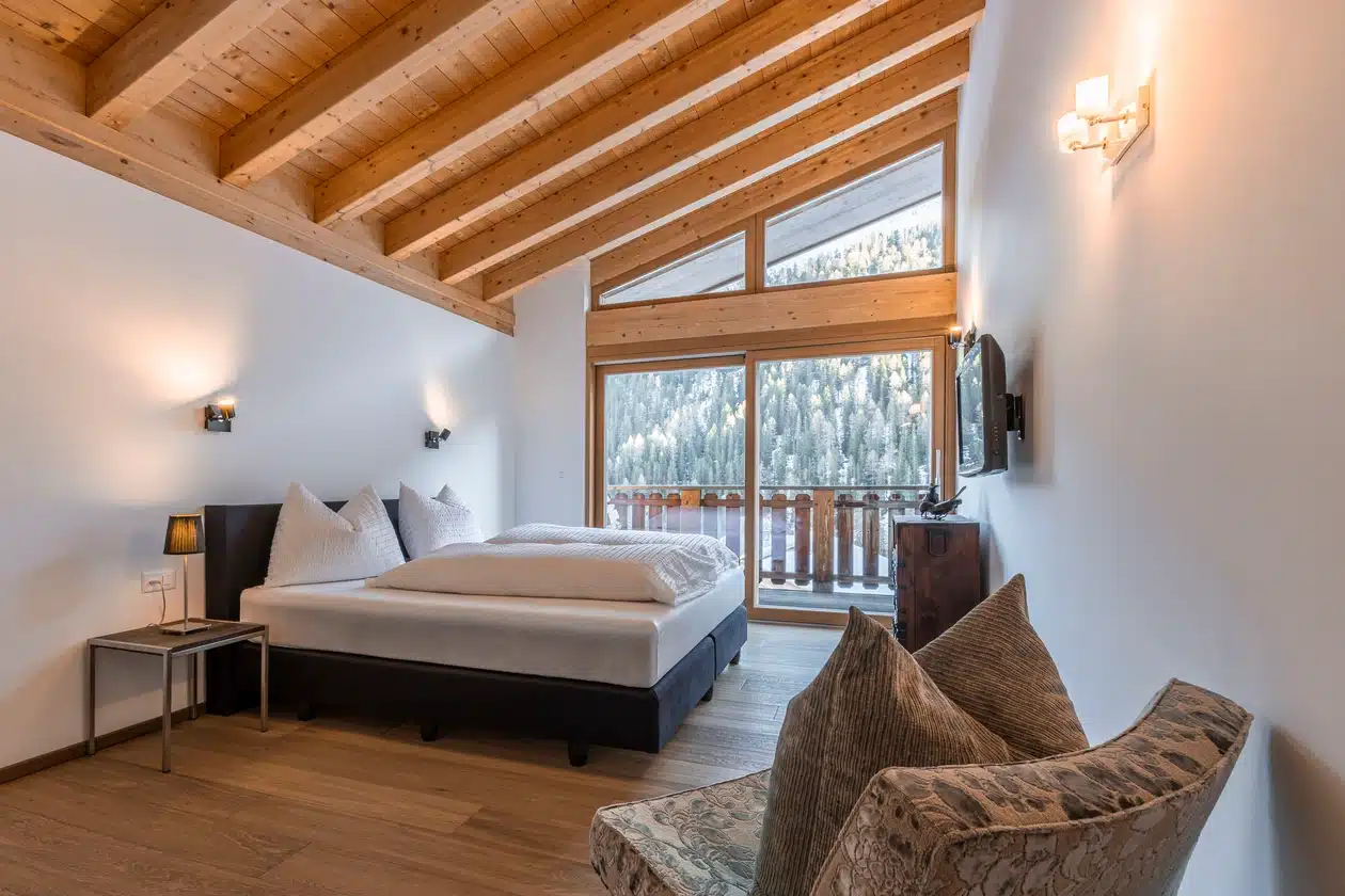 Gemütliches Schlafzimmer mit großem Bett, Sessel und Fenster mit Blick auf verschneite Berge.