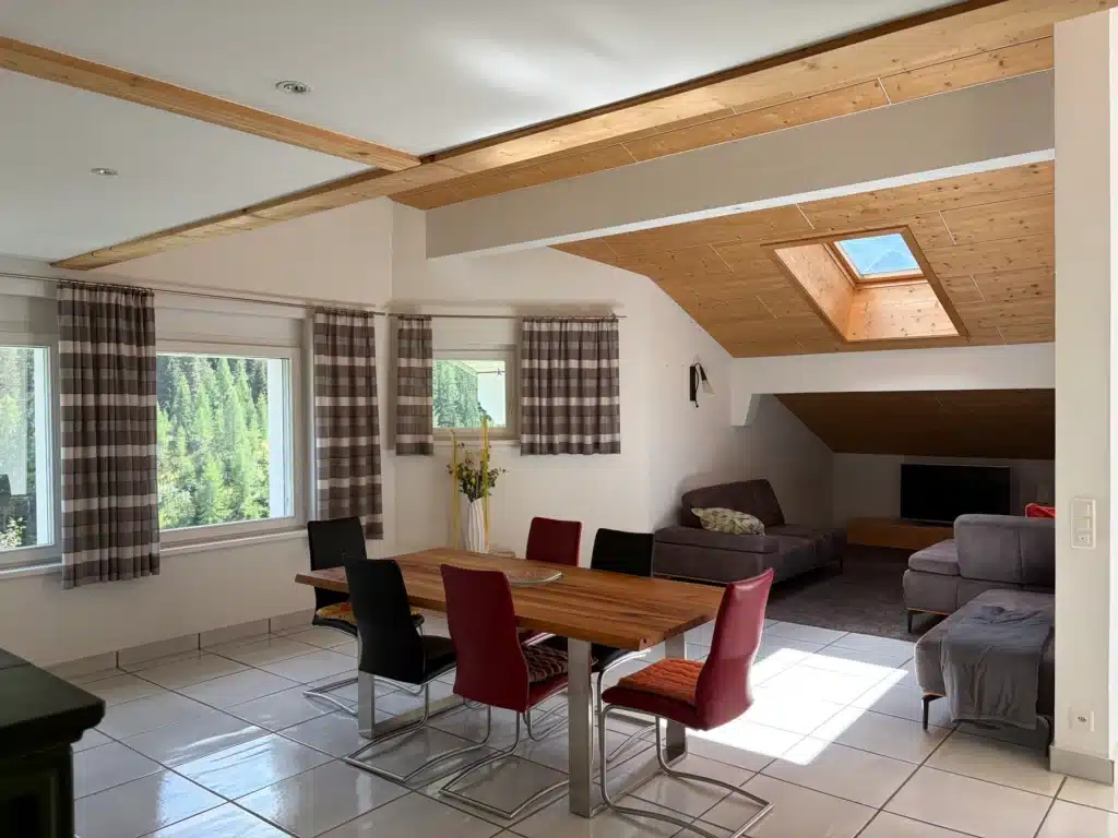 Essbereich mit Holztisch, roten und grauen Stühlen sowie Wohnzimmer mit Oberlicht und Sofas.