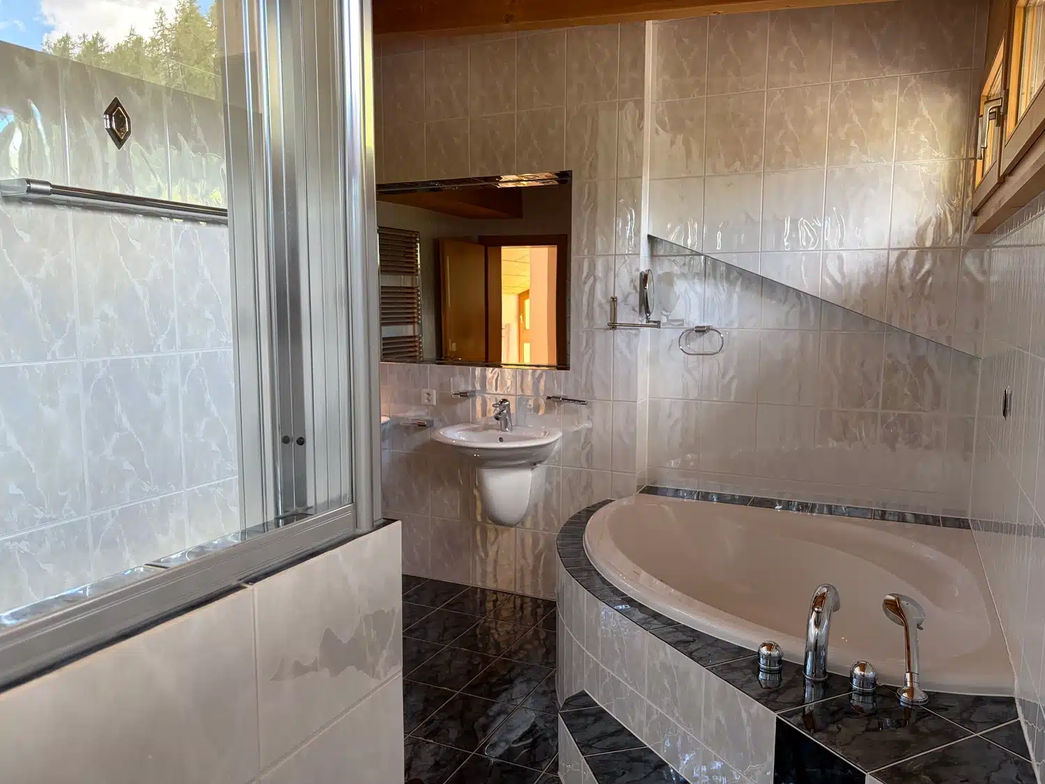 Modernes Badezimmer mit Badewanne, Waschbecken, Spiegel sowie gefliesten Wänden und Boden.