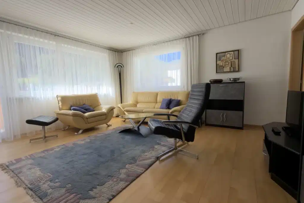 Wohnzimmer der modernen Ferienwohnung in Samnaun mit gelben Sofas, einem schwarzen Sessel und großen Fenstern.